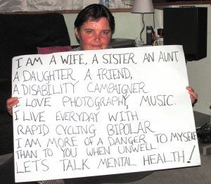 Paula Peters holding a banner - "I am a wife, a sister, an aunt, a daughter, a friend, a disability campaigner. I love photography, music, I live everyday with rapid cycling bipolar. I am more of a danger to myself than to you when unwell. Lets Talk Mental Health"