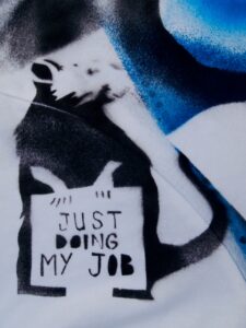 section of a handmade banner showing a rat holding a sign that says "JUST DOING MY JOB"