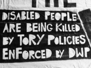 Section of a handmade banner by artist-activist Vince Laws that says "DISABLED PEOPLE ARE BEING KILLED BY TORY POLICIES ENFORCED BY DWP" 