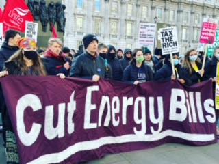 Activists are opposite Number 10 Downing Street london on the cost of living crisis Demo holding a 4 metre purple banner with white wording that says Cut Energy Bills