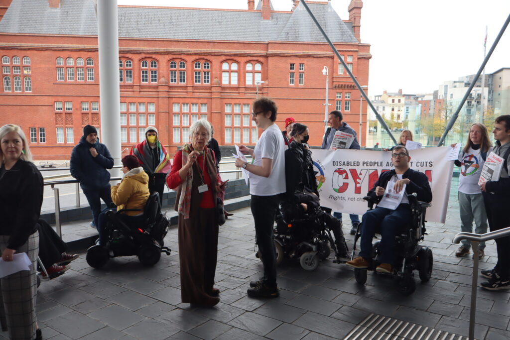 Disability campaigners from Disabled People Against Cuts Cymru at the Senedd (Welsh Parliament) talk with the politician Jenny Rathbone MS.